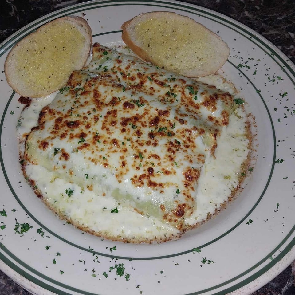 Baked manicotti covered in melted cheese and parsley, served with two slices of garlic bread.