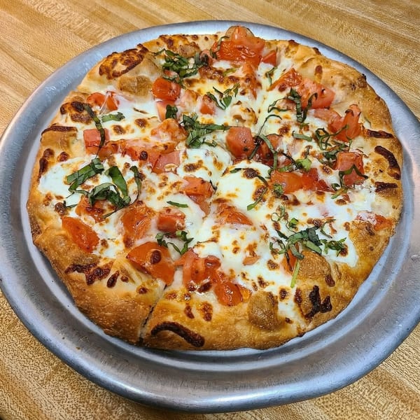 A freshly baked Margherita pizza with melted mozzarella, diced tomatoes, and fresh basil on a metal tray.