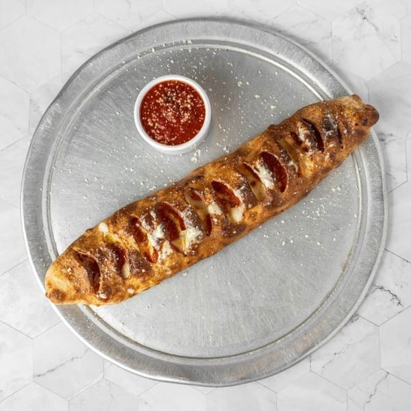 A pepperoni stromboli with melted cheese and a side of marinara sauce on a metal pizza pan.