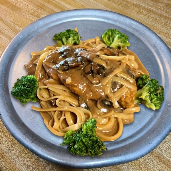Creamy mushroom pasta with chicken and broccoli florets on a silver plate.